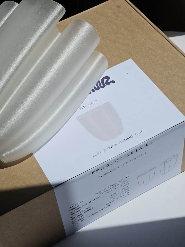 The finished Flo lamp in sunlight on its box, with the product details label
