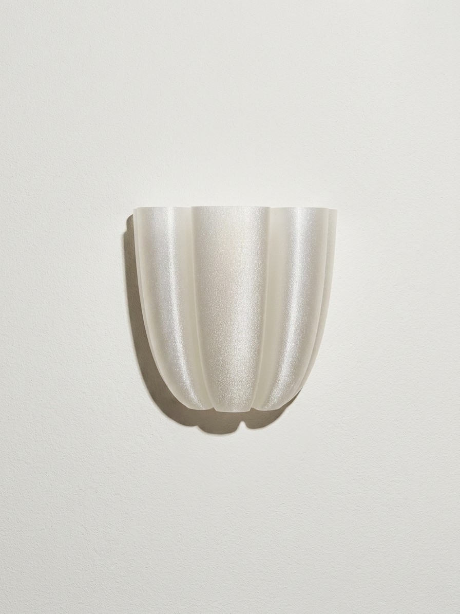 The Flo lamp on a white wall, its fluted, softly glittering surface finished by hand